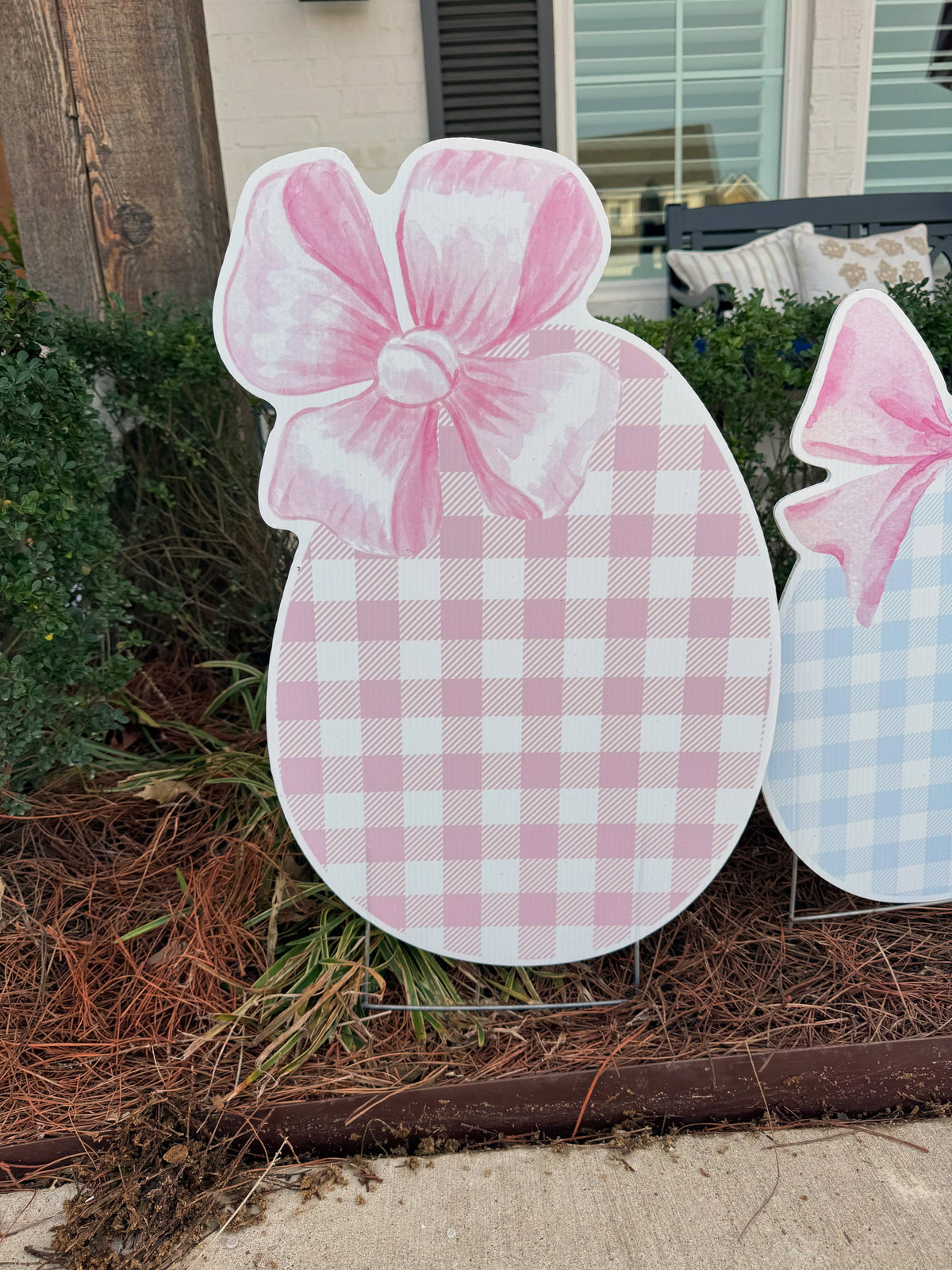 Decorative Easter egg with a pink bow on a stand outdoors.