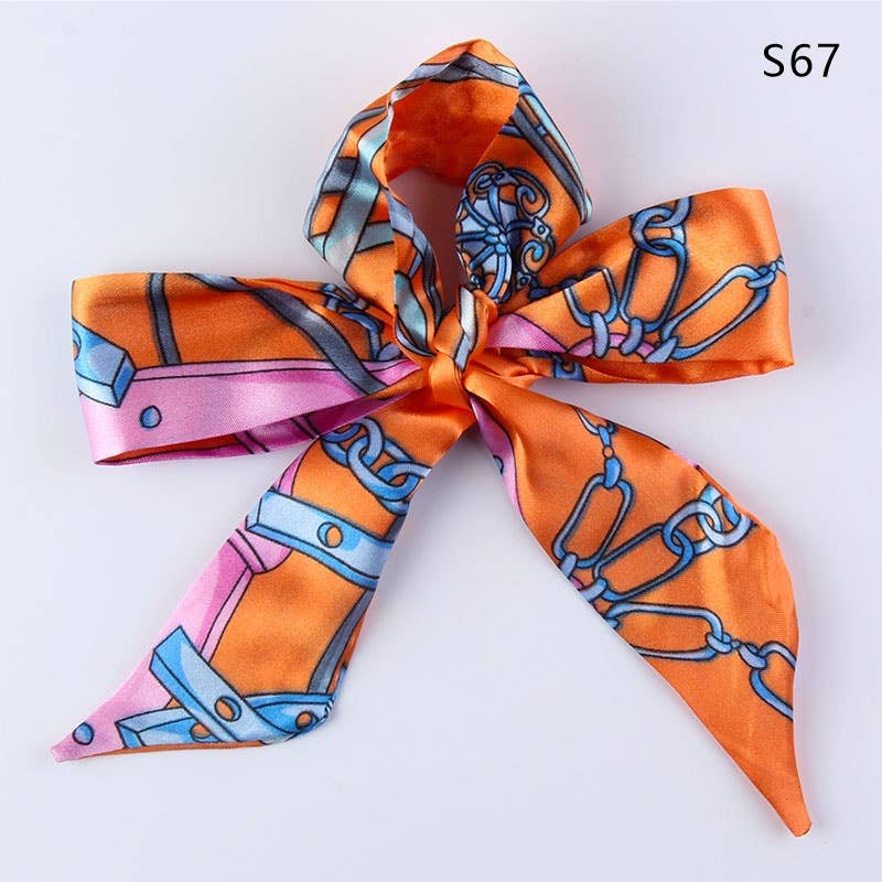 An orange silk scarf tied into a bow, featuring a colorful print of pink, light blue, and gray chain links and geometric shapes, shown on a plain white background with the text 'S67' in the top right corner.