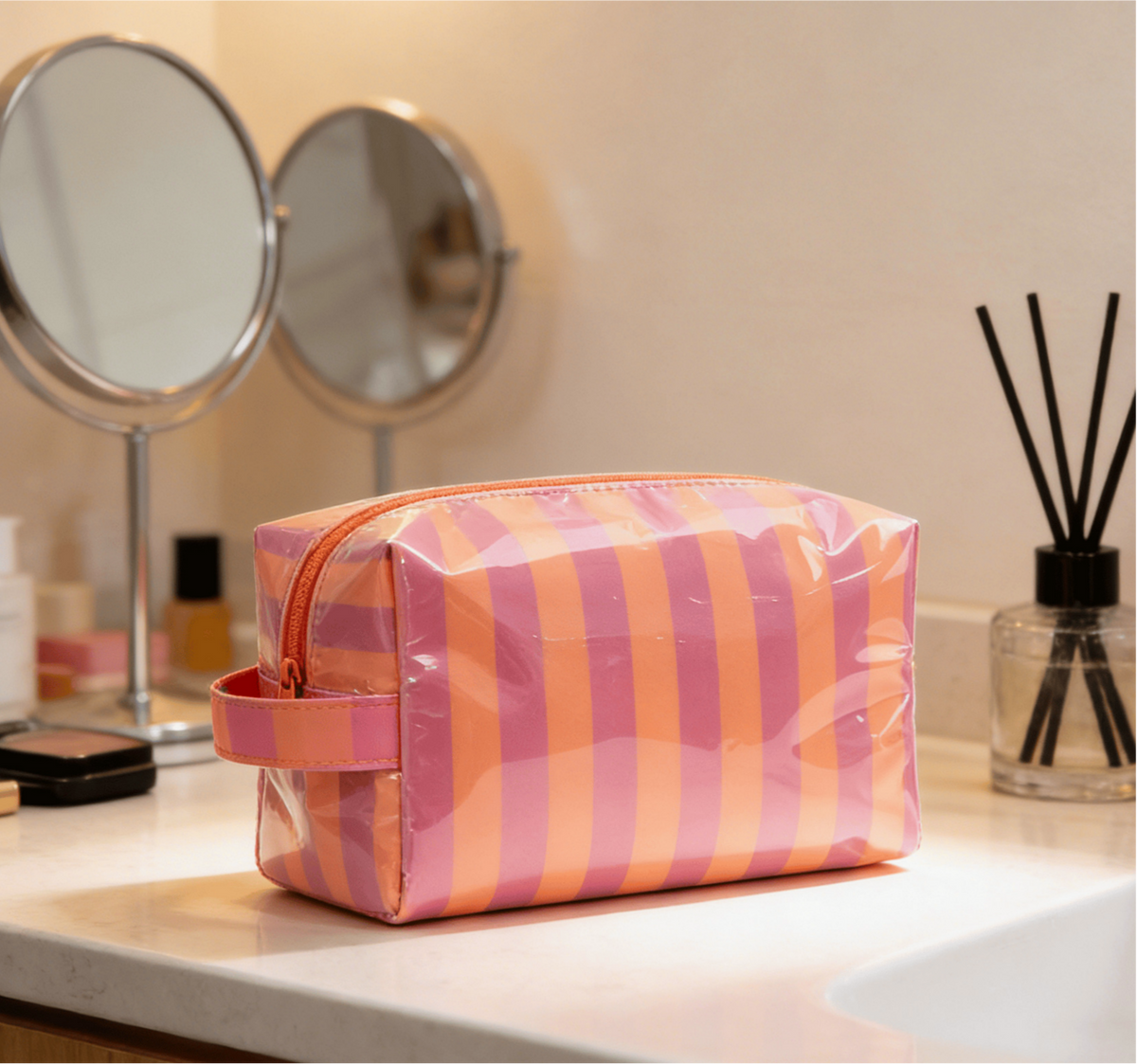 Pink and orange striped toiletry bag on a bathroom counter with mirrors and a diffuser in the background.