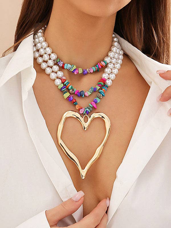 Gold heart-shaped pendant necklace on a person wearing a white shirt.