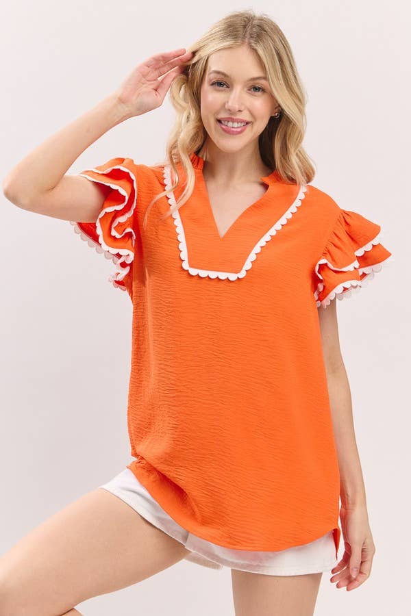 Woman wearing an orange top with white trim on a plain background