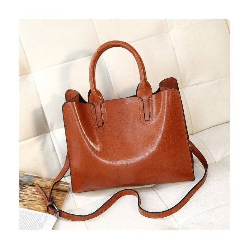A brown leather handbag with double top handles and a detachable shoulder strap, resting on a cream-colored tufted sofa.