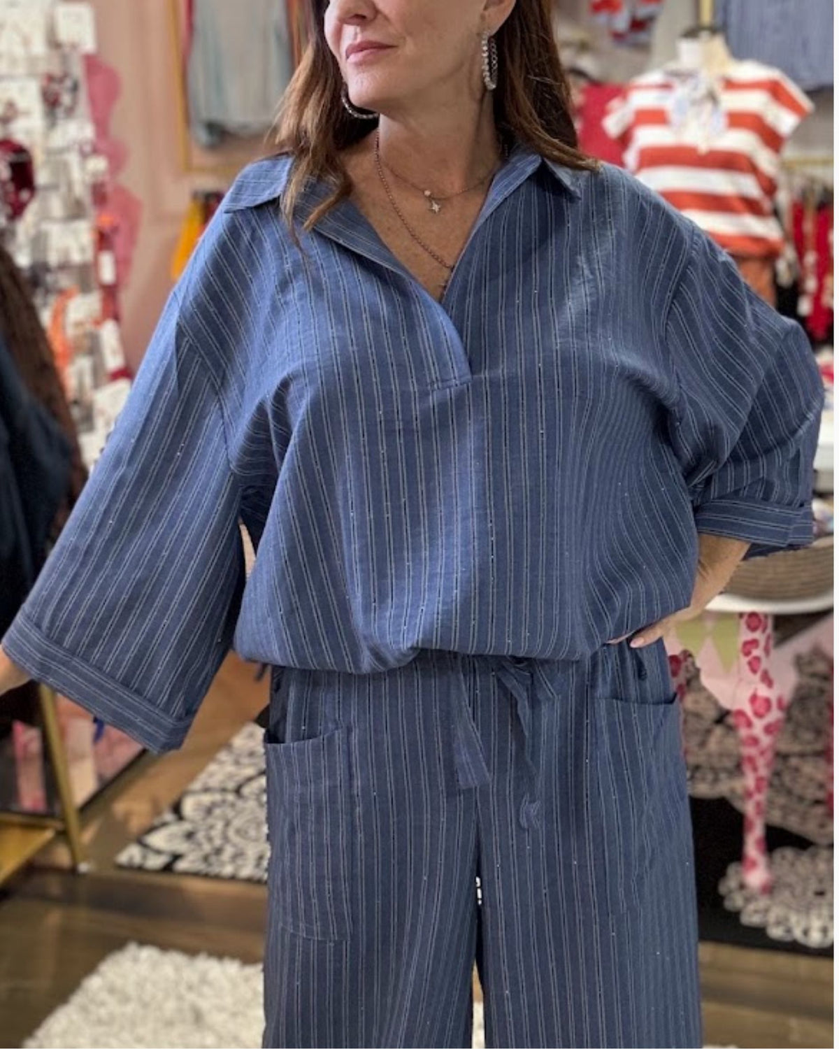 A woman wearing a matching blue pinstriped lounge set with a collared short-sleeve top and wide-leg pants, standing in a retail store.