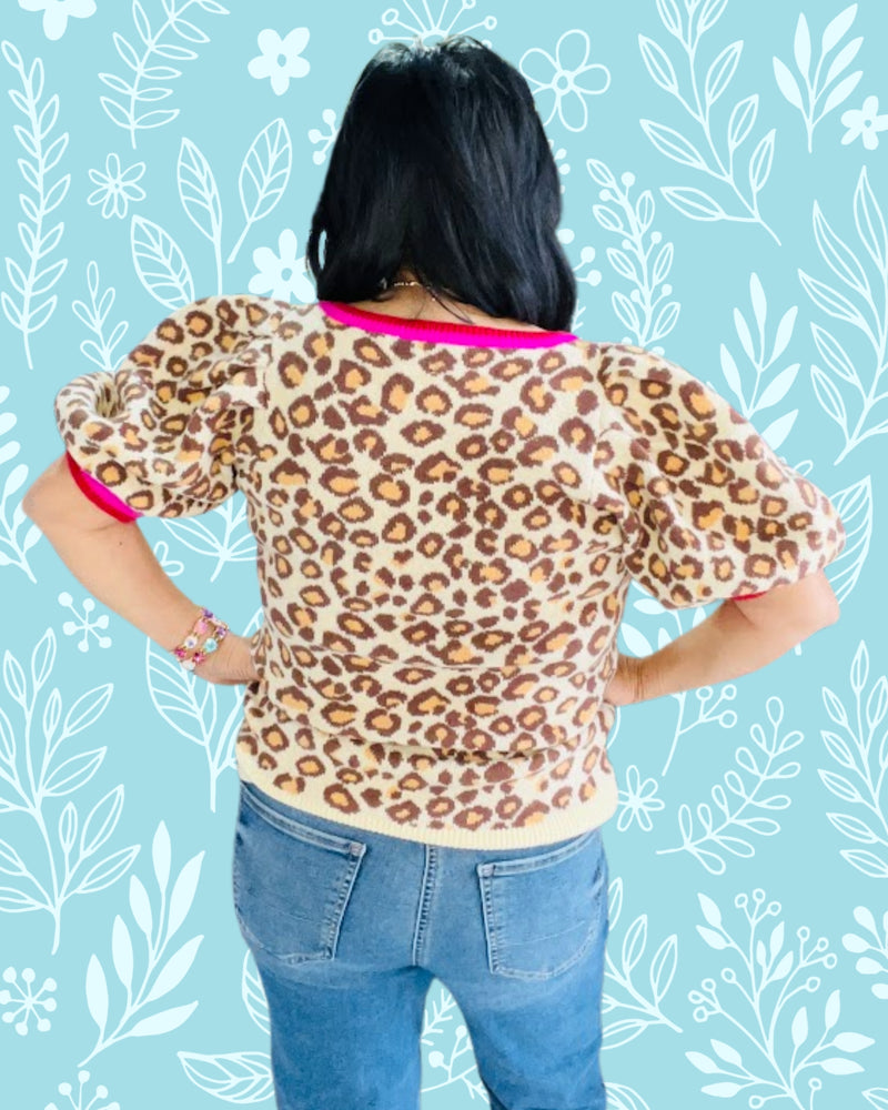 Person wearing a leopard print top with pink trim against a blue floral patterned background