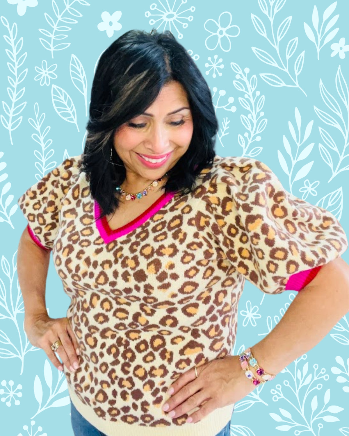 Woman wearing a leopard print top with pink trim against a light blue background with white floral patterns.