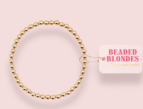 Gold beaded bracelet on a pink background with 'Beaded Blondes' branding.