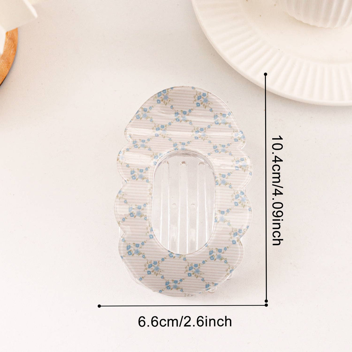 A clear scalloped acrylic dish or tray with a blue floral pattern, shown with black measurement lines and text indicating dimensions of 10.4cm by 6.