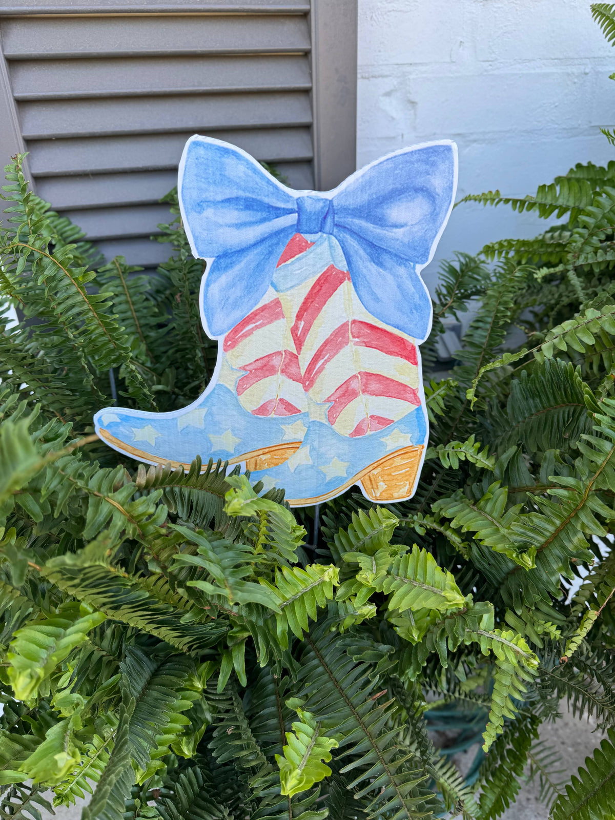 Decorative boot with a blue bow and American flag design on green foliage.