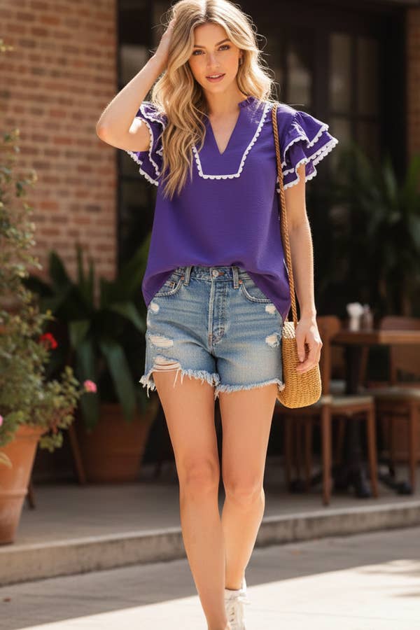 Woman wearing a purple blouse and denim shorts standing outdoors.