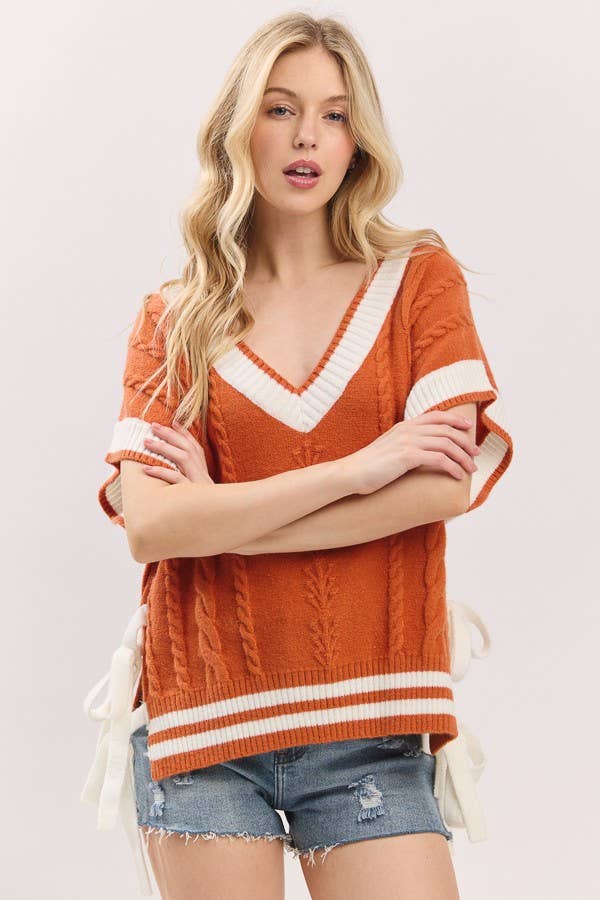 Woman wearing an orange sweater with white trim and denim shorts on a light background
