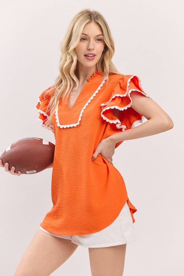 Woman wearing an orange ruffled top holding a football on a plain background