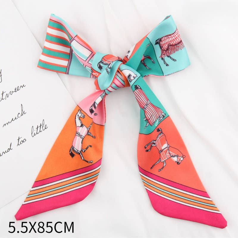 A square silk scarf tied into a large bow, featuring a colorful print of horses on bright orange, pink, and turquoise backgrounds with striped accents. The scarf is displayed on a white fabric background next to a decorative card with cursive text, with a size overlay '5.