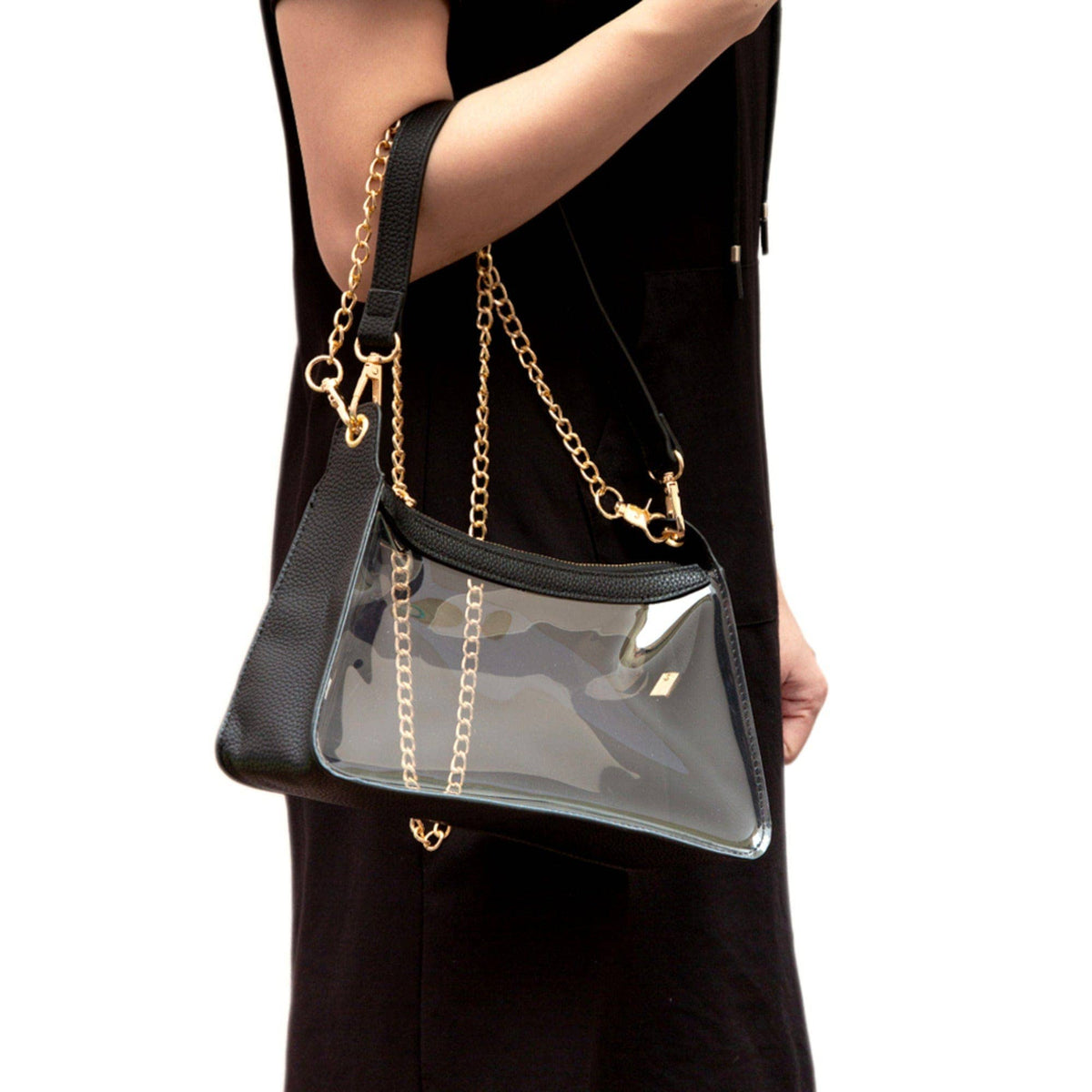 Black handbag with gold chain strap held by a person wearing a black outfit on a white background