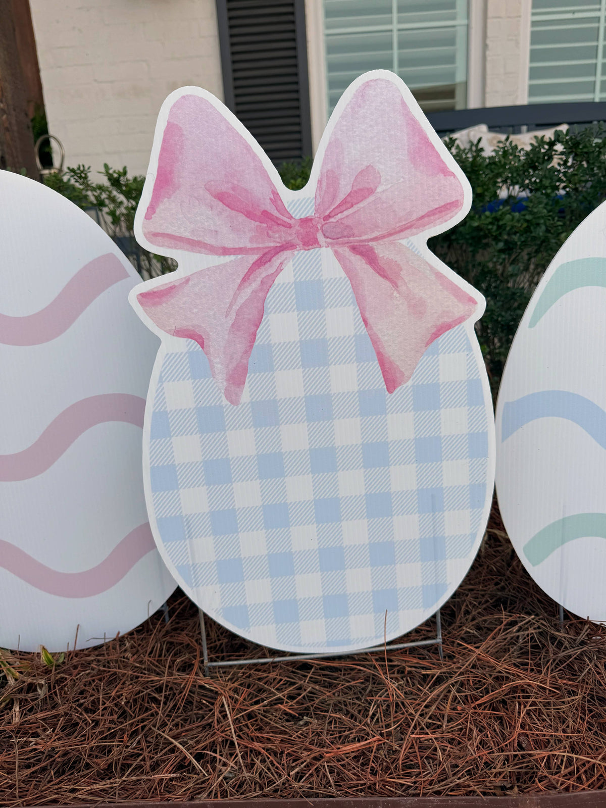 Decorative Easter egg with a pink bow on a stand outdoors.
