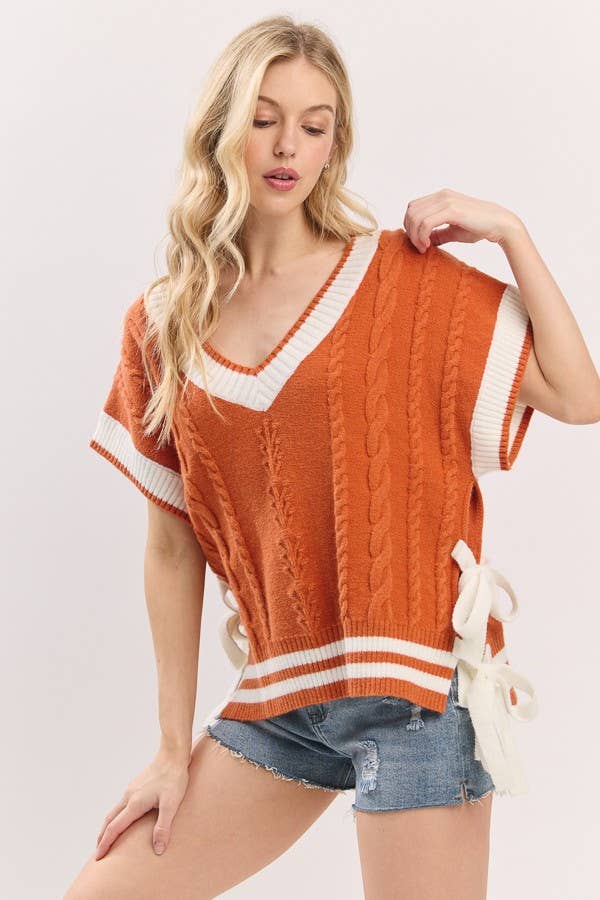 Woman wearing an orange and white sweater with denim shorts on a light pink background
