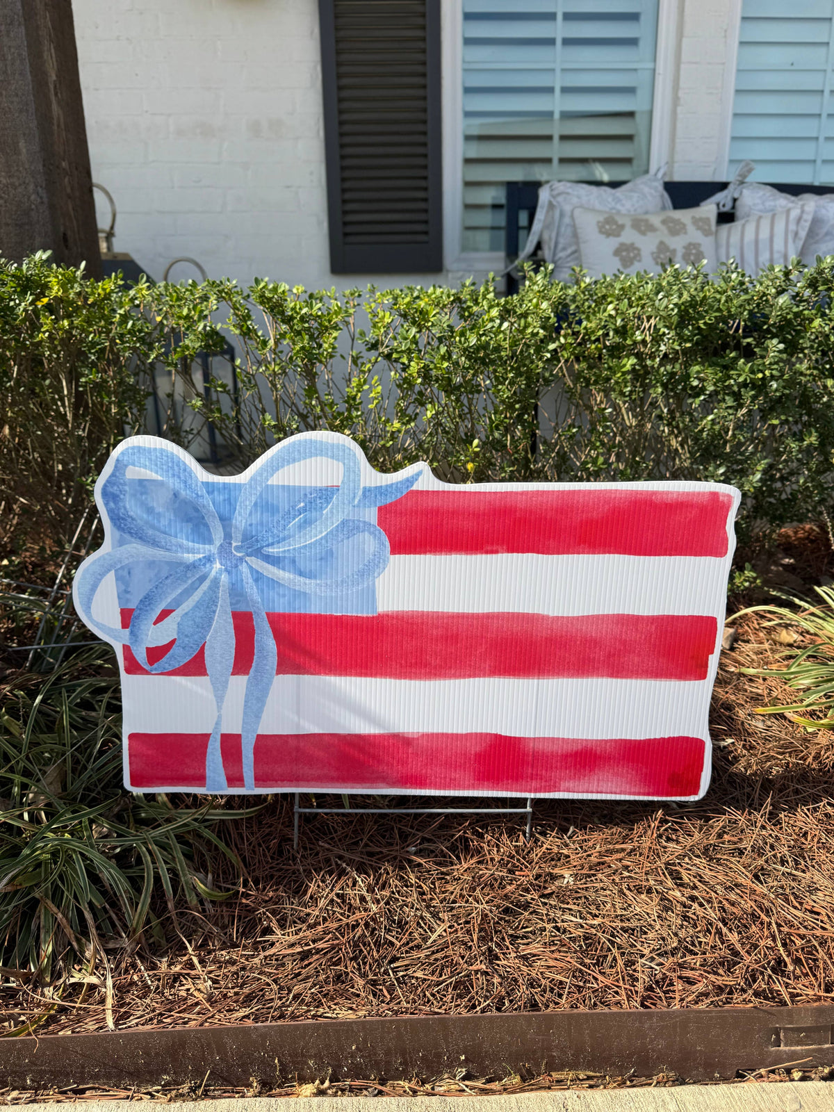 Decorative sign with red and white stripes and a blue bow in front of a house.