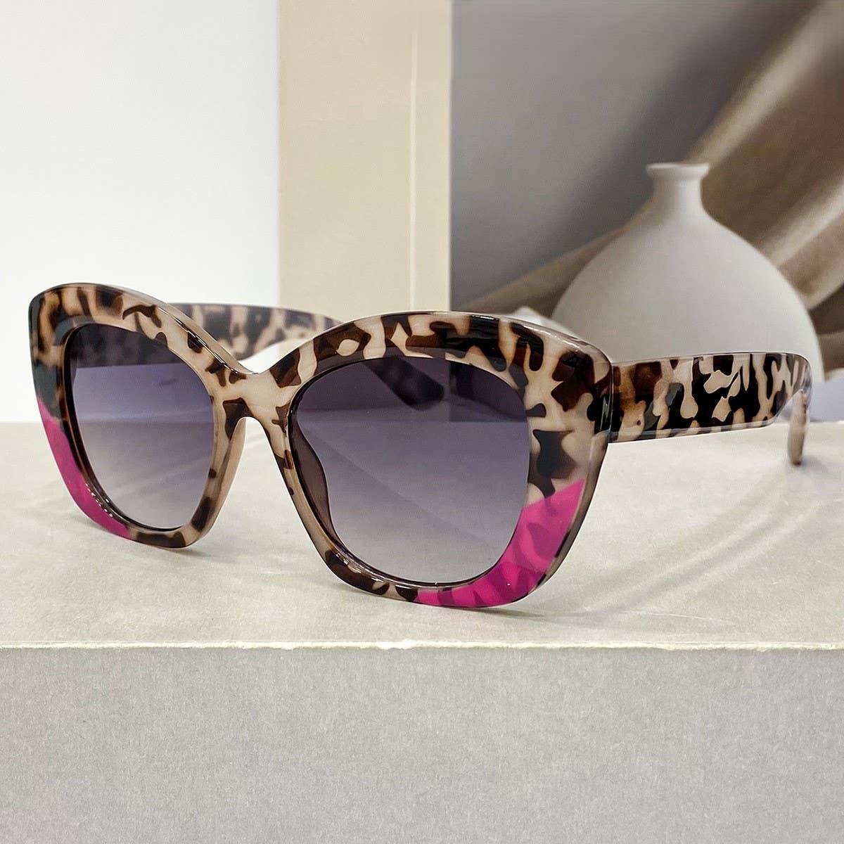 Sunglasses with leopard print and pink accents on a light surface.