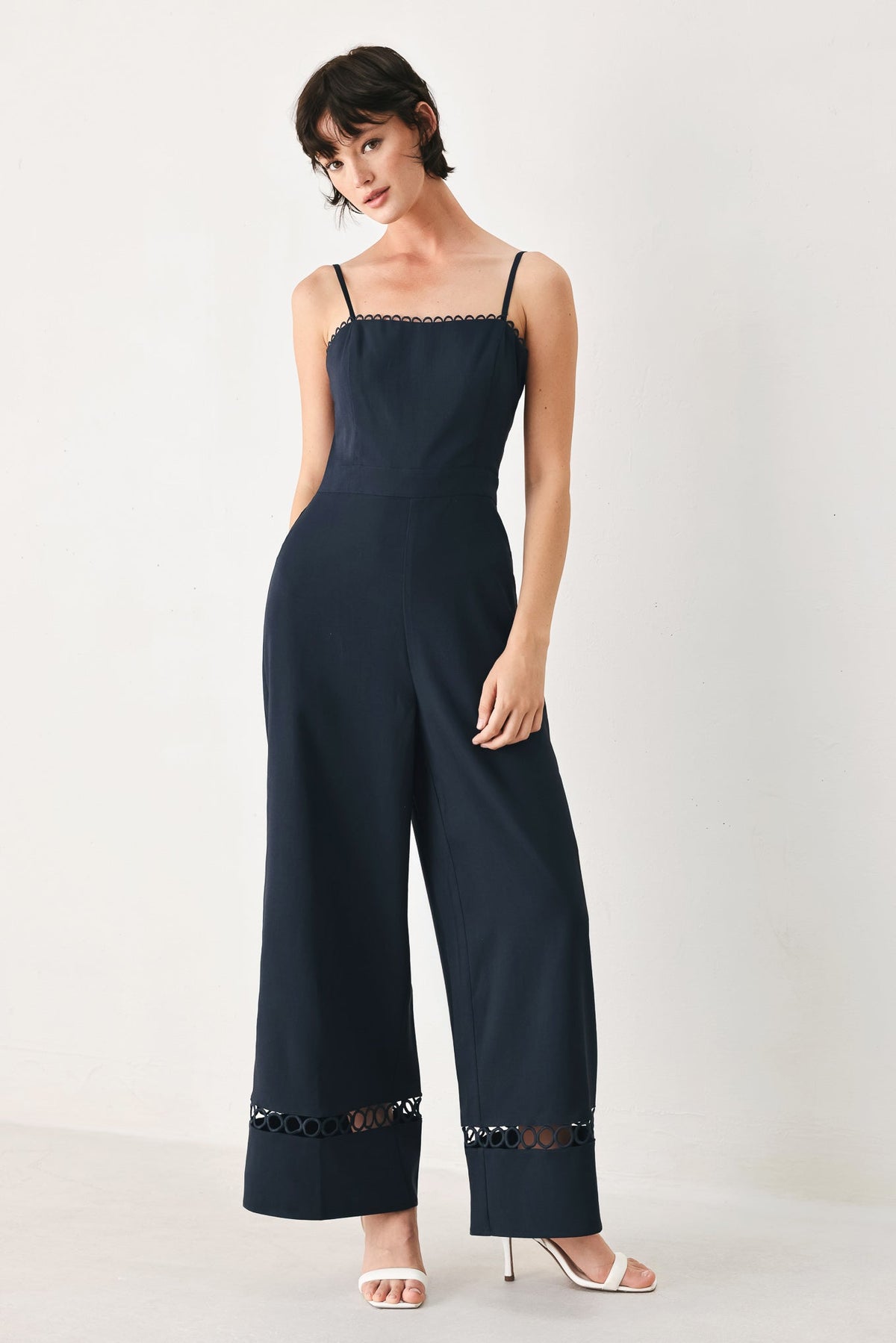 Woman wearing a navy jumpsuit with lace details on a white background