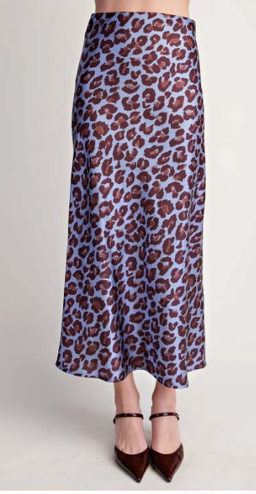 A model is shown from the waist down wearing a light blue satin midi skirt with a brown leopard print pattern, paired with dark brown pointed-toe heels.