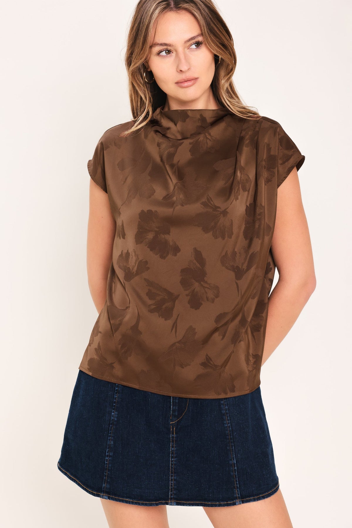 Woman wearing a brown floral sleeveless top and denim skirt on a white background