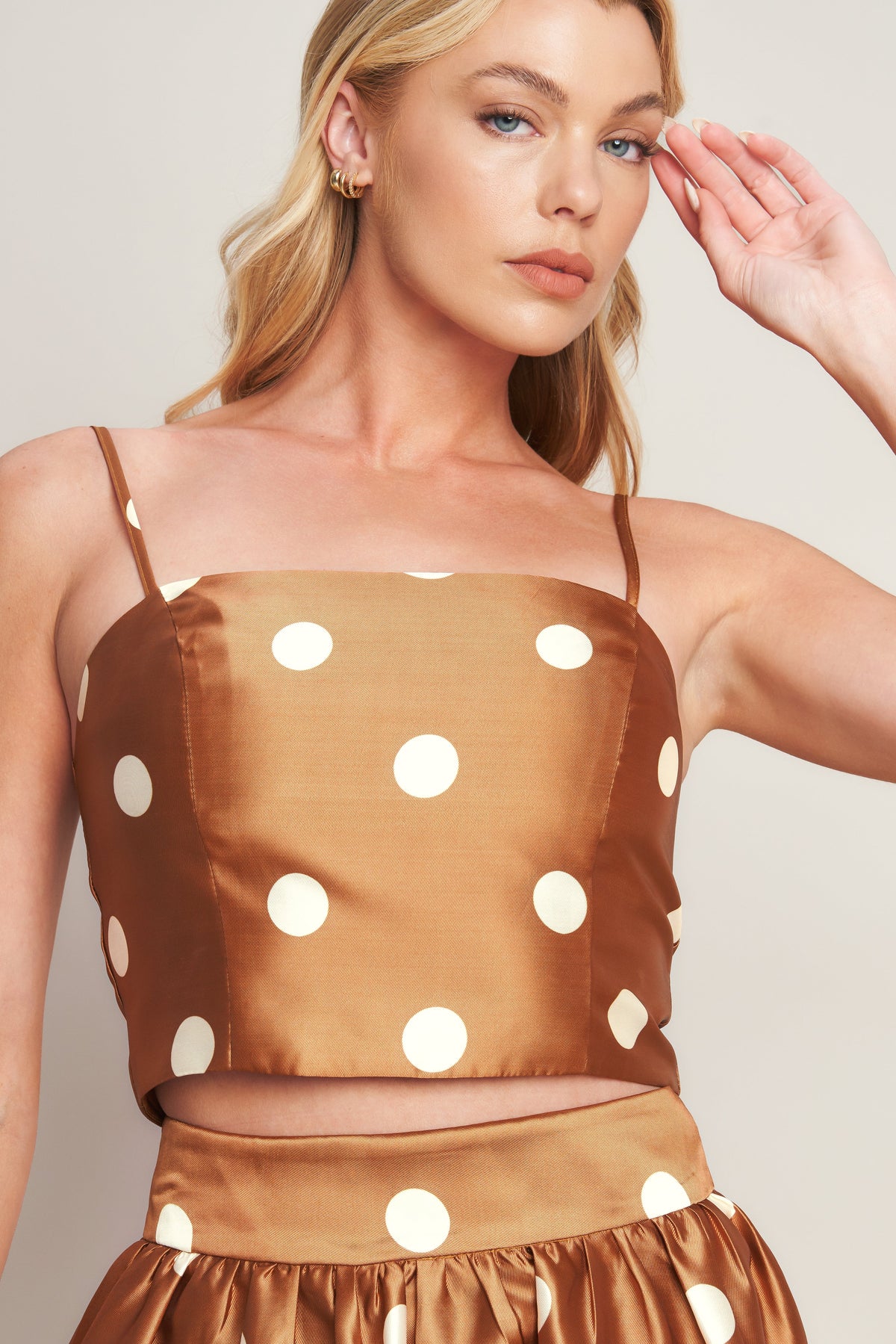 Woman wearing a brown polka dot top against a plain background