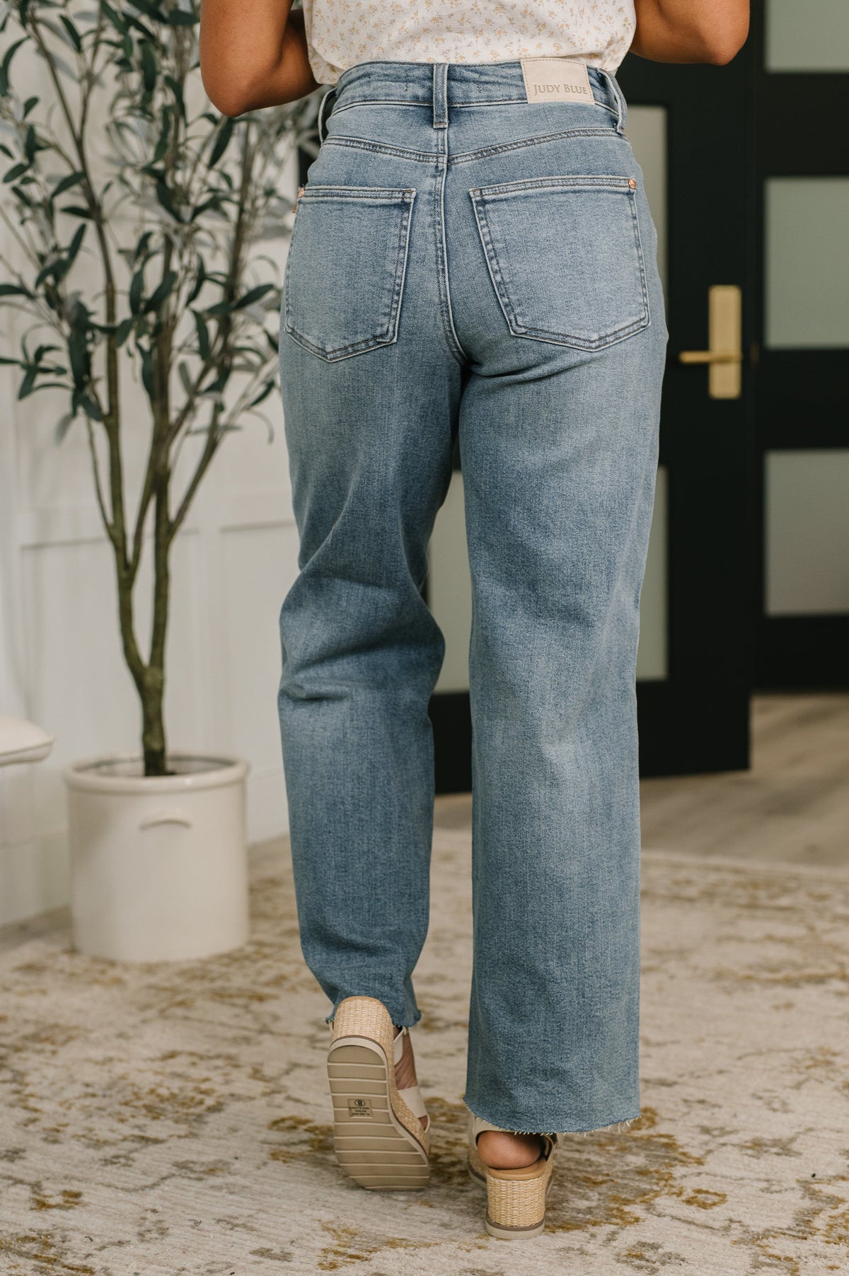 Person wearing blue jeans standing in a room with a plant and door in the background