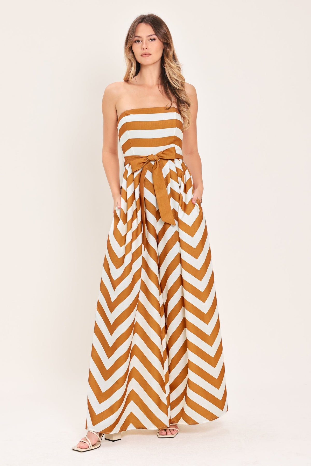 Woman wearing a strapless dress with brown and white chevron pattern on a plain background