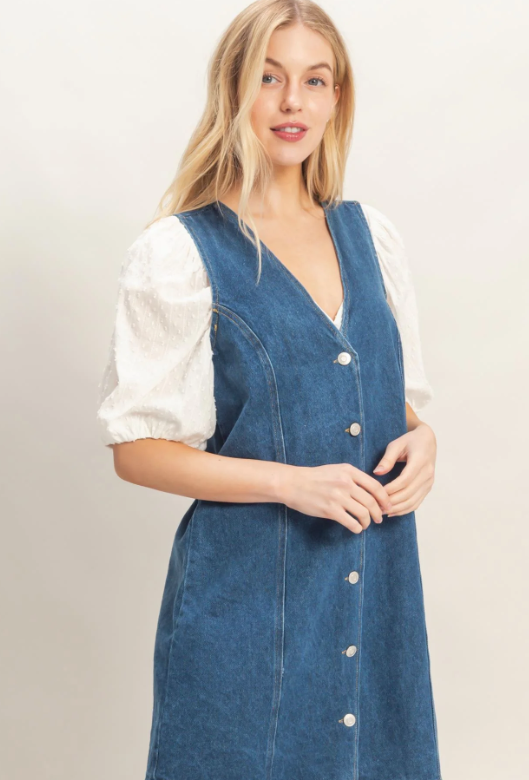 Woman wearing a blue denim dress over a white shirt against a plain background