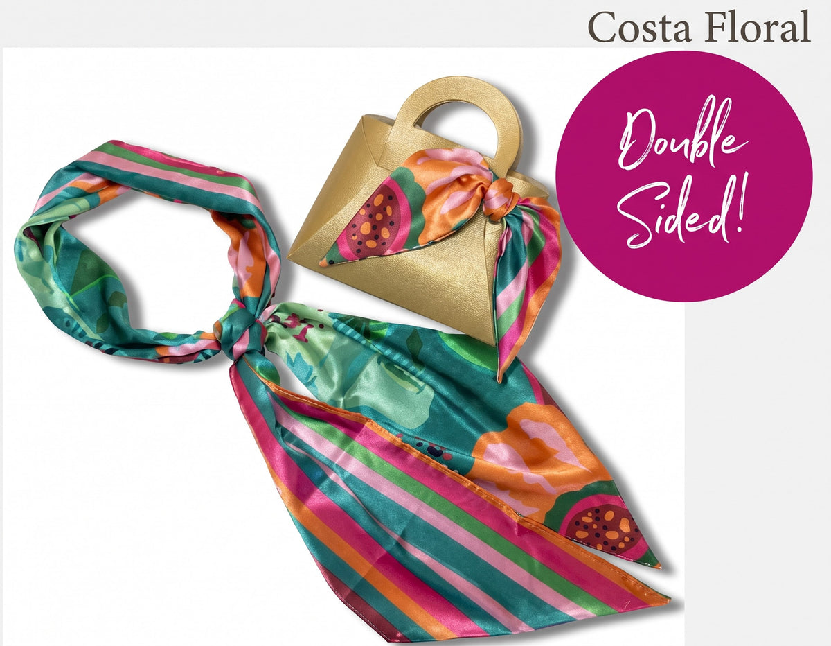 A double-sided silk scarf in a Costa Floral print, styled with a gold paper bag and a matching small fabric bag, with a magenta circular badge reading 'Double Sided!' and text 'Costa Floral' at the top.