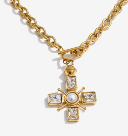 Gold cross pendant necklace featuring a central white pearl and four clear rectangular crystals, suspended from a thick gold chain on a light gray background.