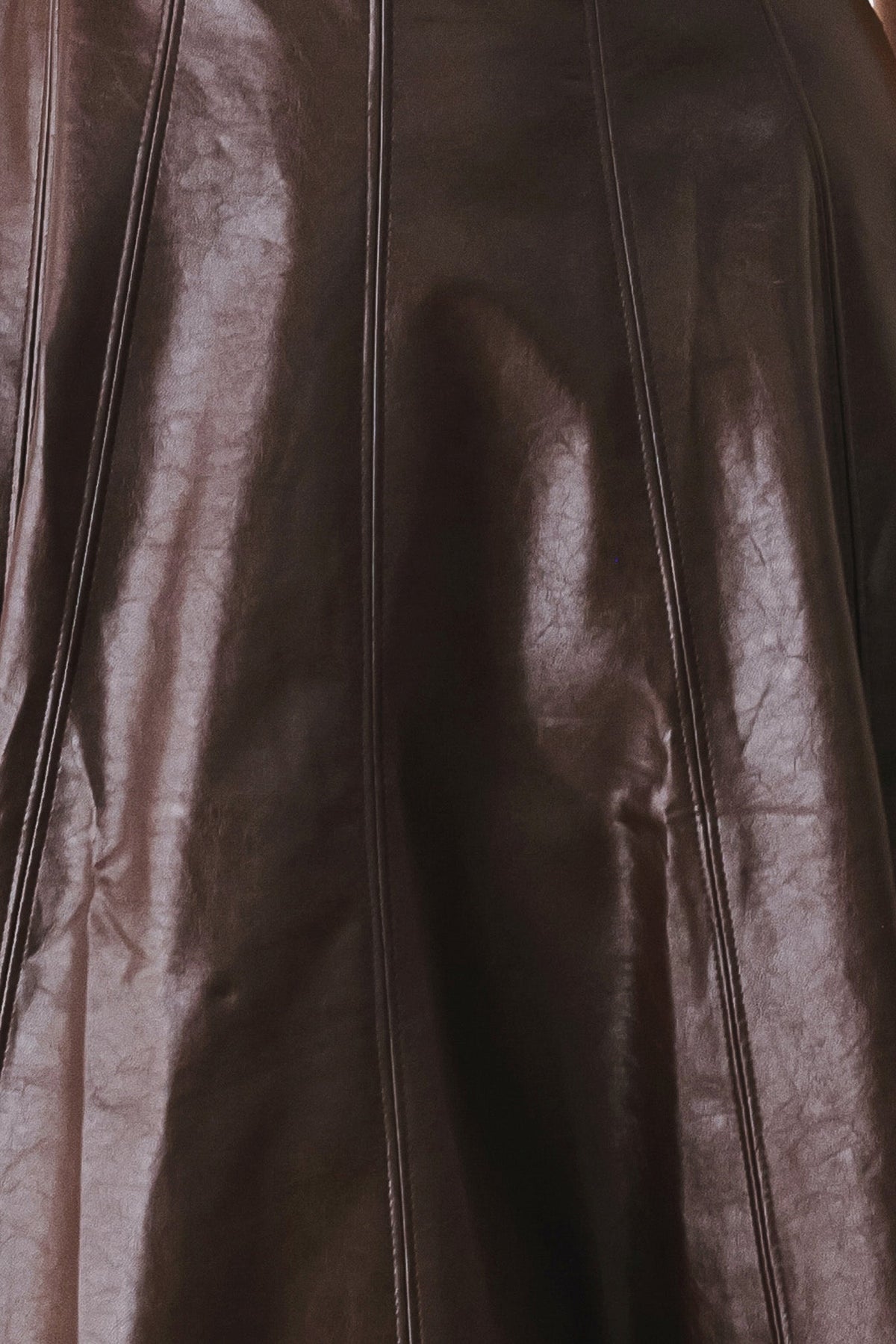 Close-up of a dark brown leather garment with vertical seam detailing and a glossy finish.