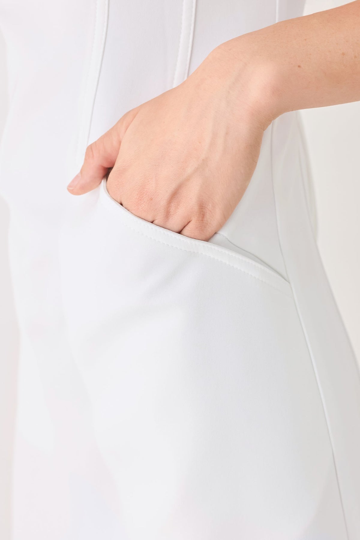 Close-up of a person's hand in a white sleeveless top with a plain background