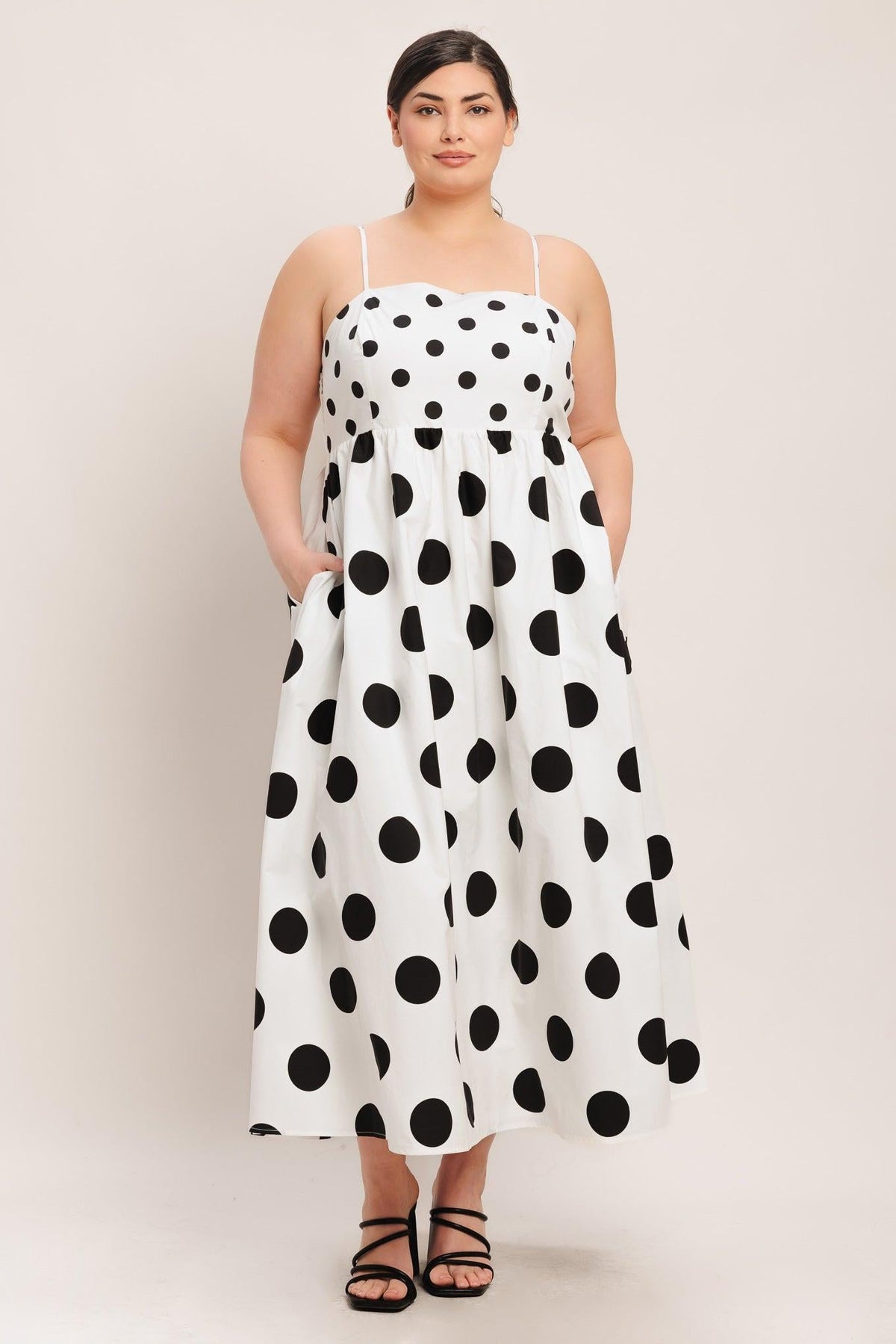 Woman wearing a white dress with black polka dots against a plain background