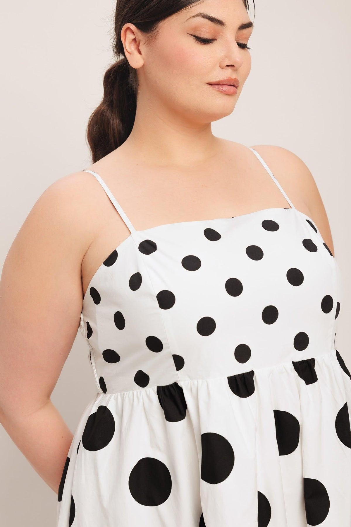 Woman wearing a white dress with black polka dots against a plain background
