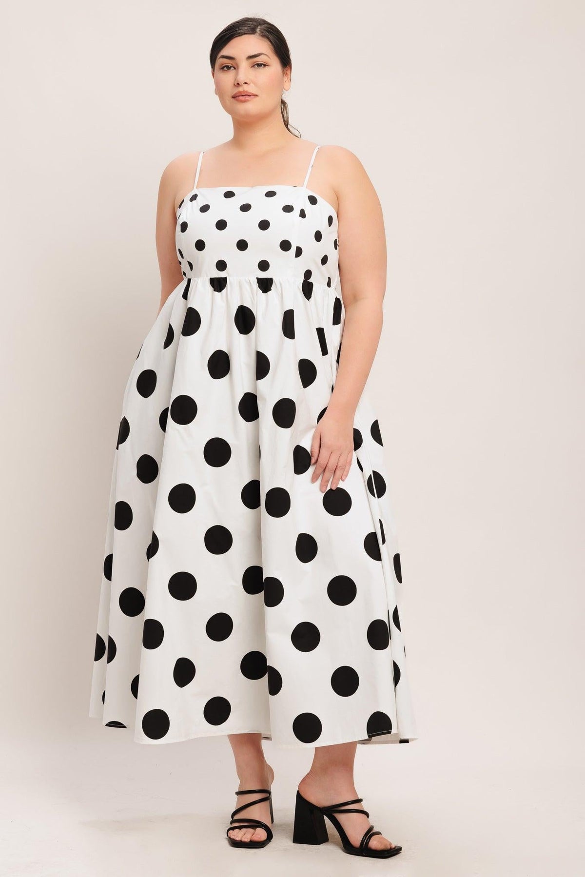Woman wearing a white dress with black polka dots on a plain background