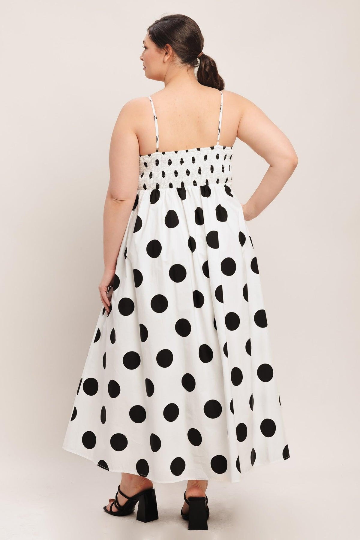 Woman wearing a white dress with black polka dots against a plain background