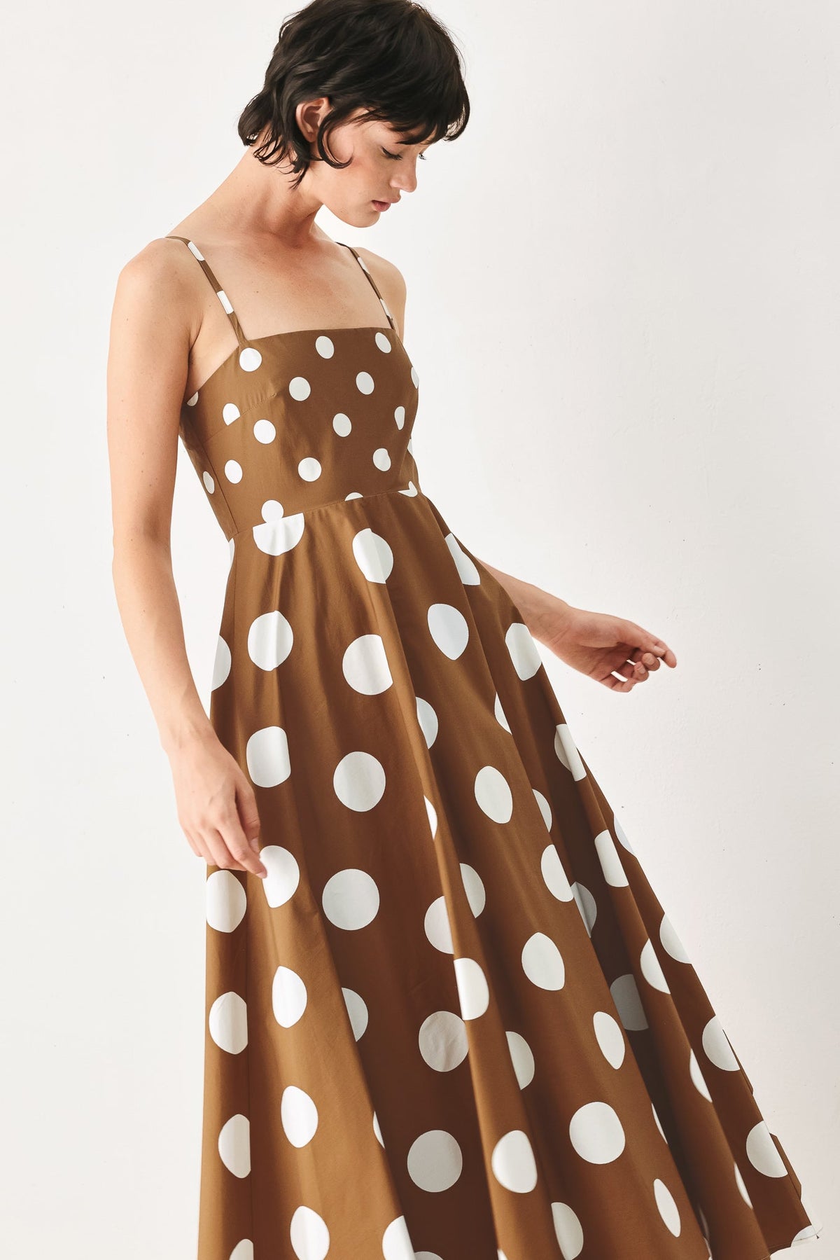 Woman wearing a brown dress with white polka dots on a white background