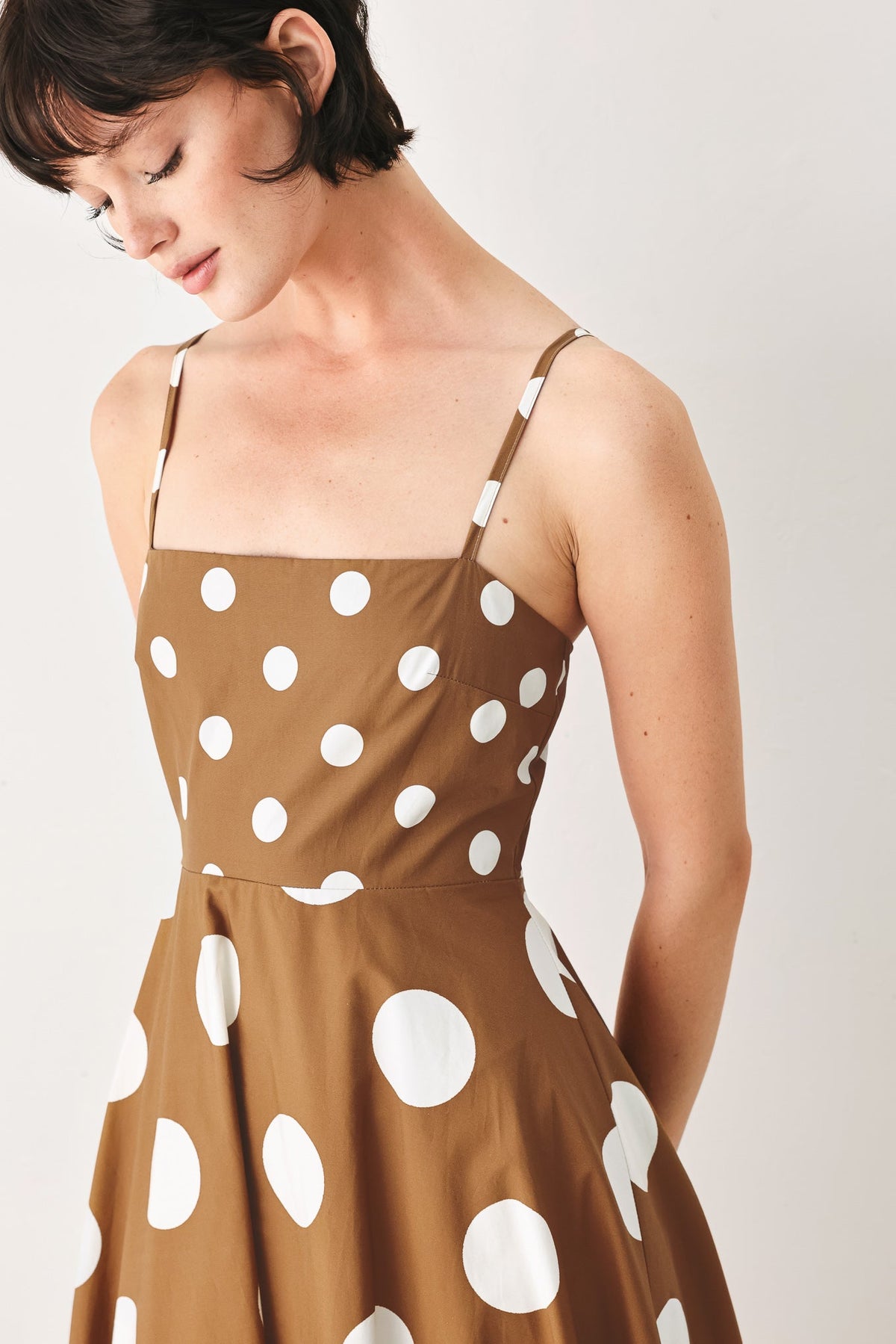 Woman wearing a brown dress with white polka dots against a plain background