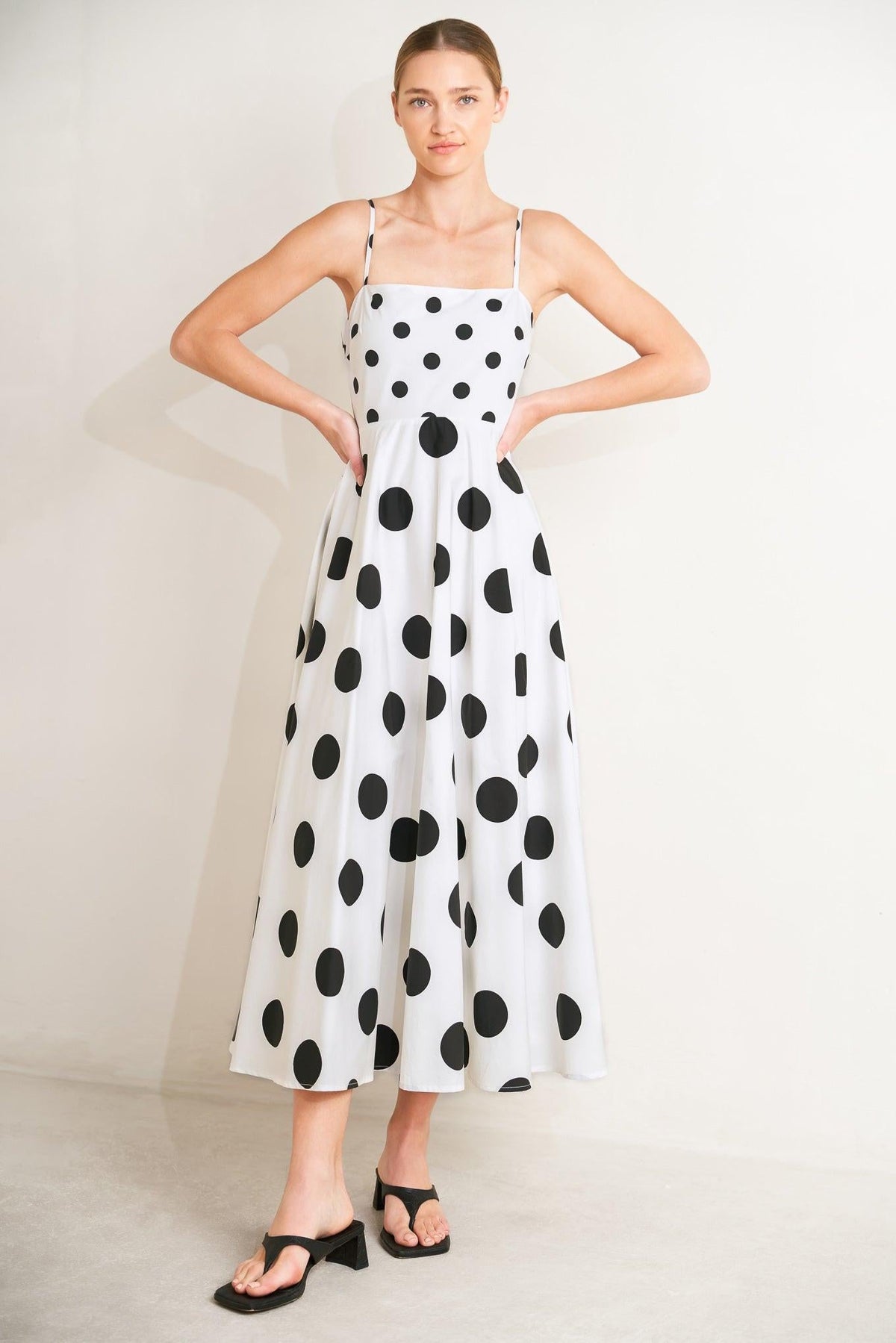 Woman wearing a white dress with black polka dots on a plain background