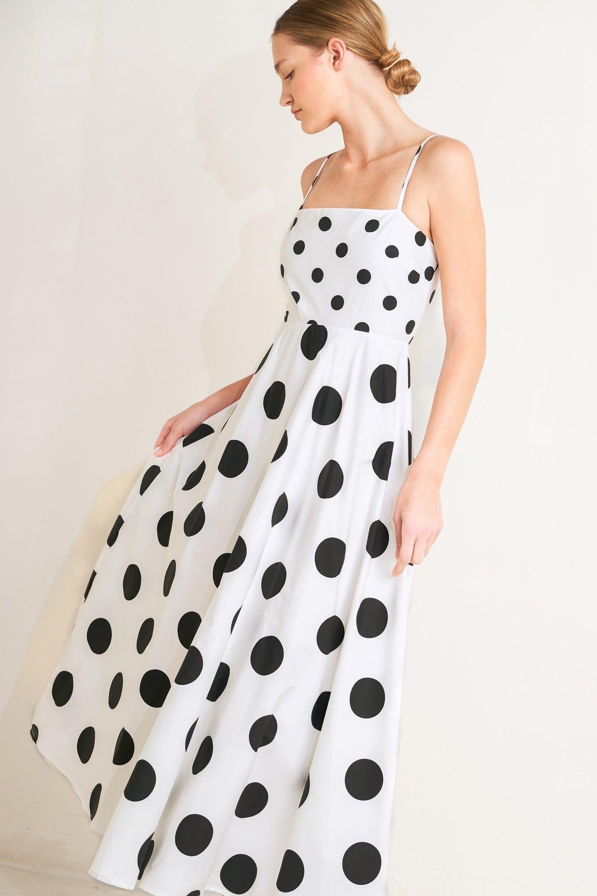 Woman wearing a white dress with black polka dots against a plain background
