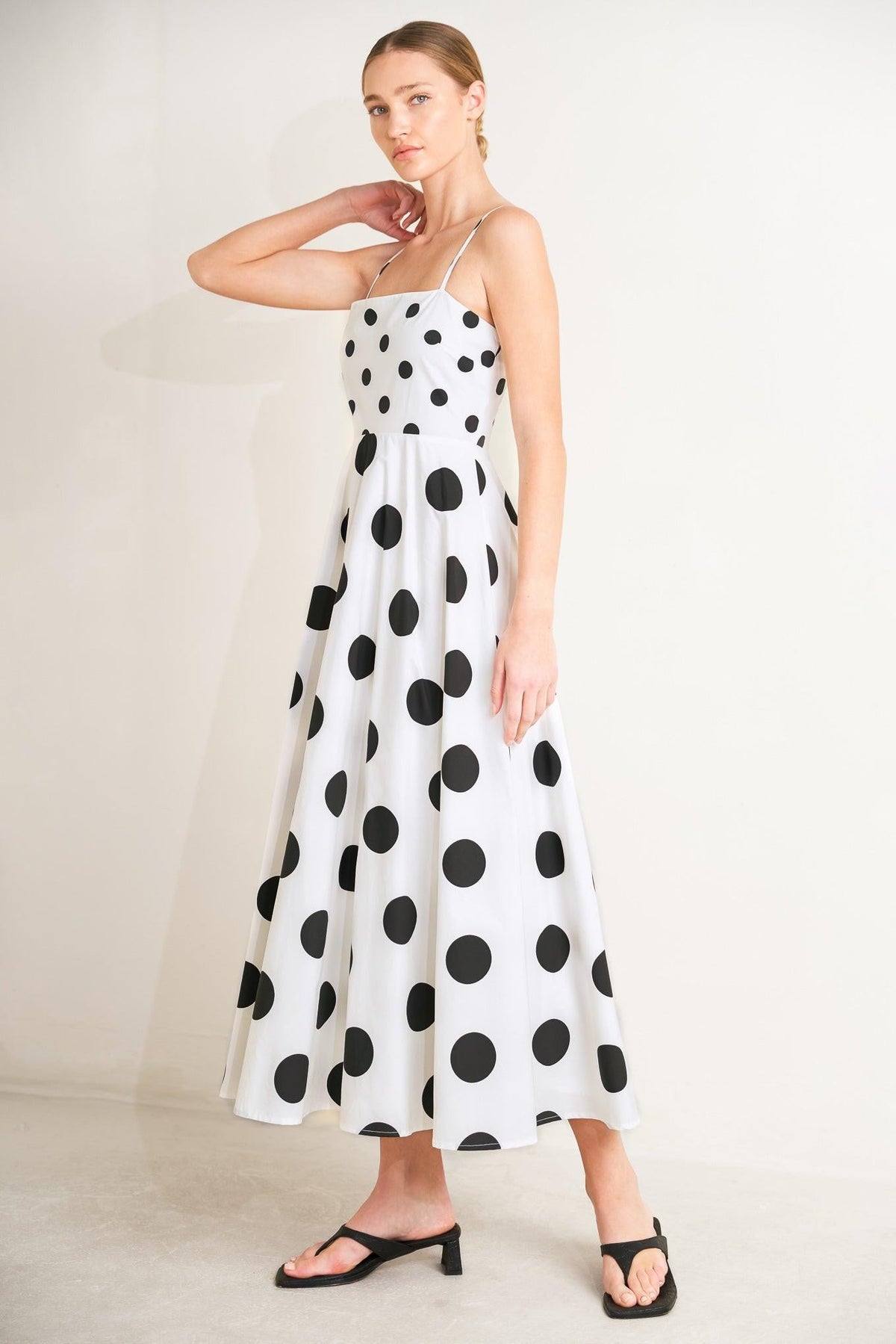 Woman wearing a white dress with black polka dots on a plain background