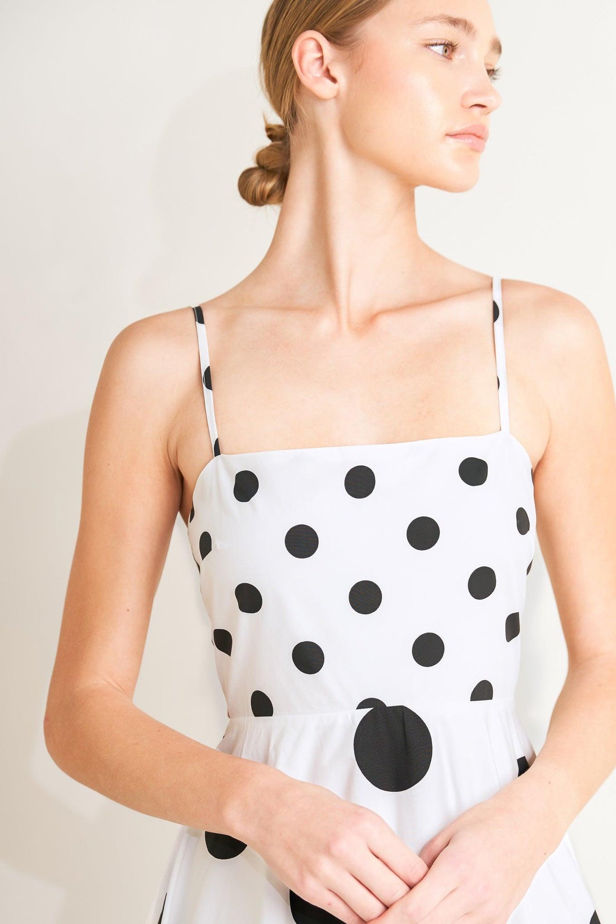 Woman wearing a white dress with black polka dots against a plain background