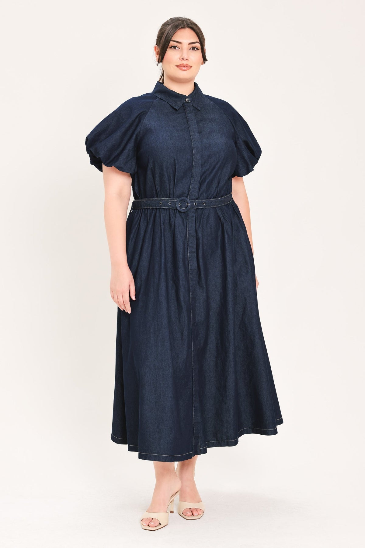 A woman modeling a dark navy blue midi shirt dress with puff sleeves, a pointed collar, and a matching fabric belt, set against a plain light background.