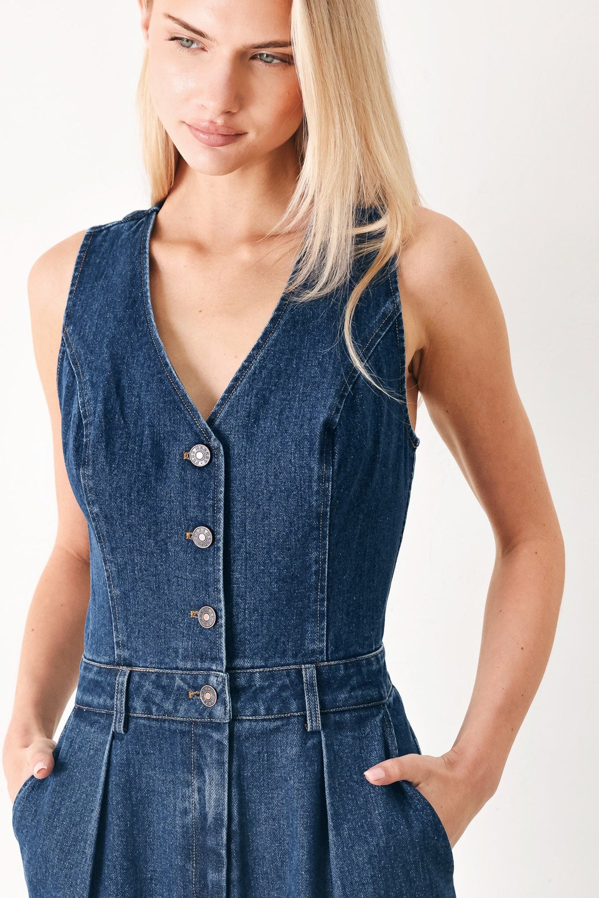 Woman wearing a blue denim dress with buttons on a white background