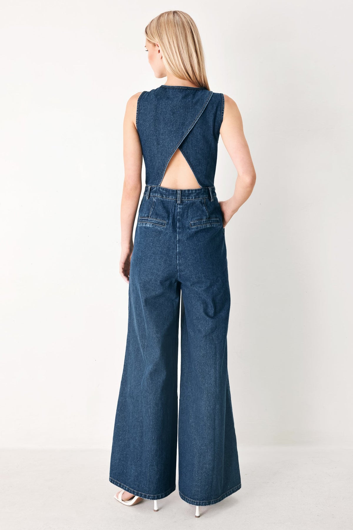 Woman wearing a blue denim jumpsuit with a cutout back design on a white background