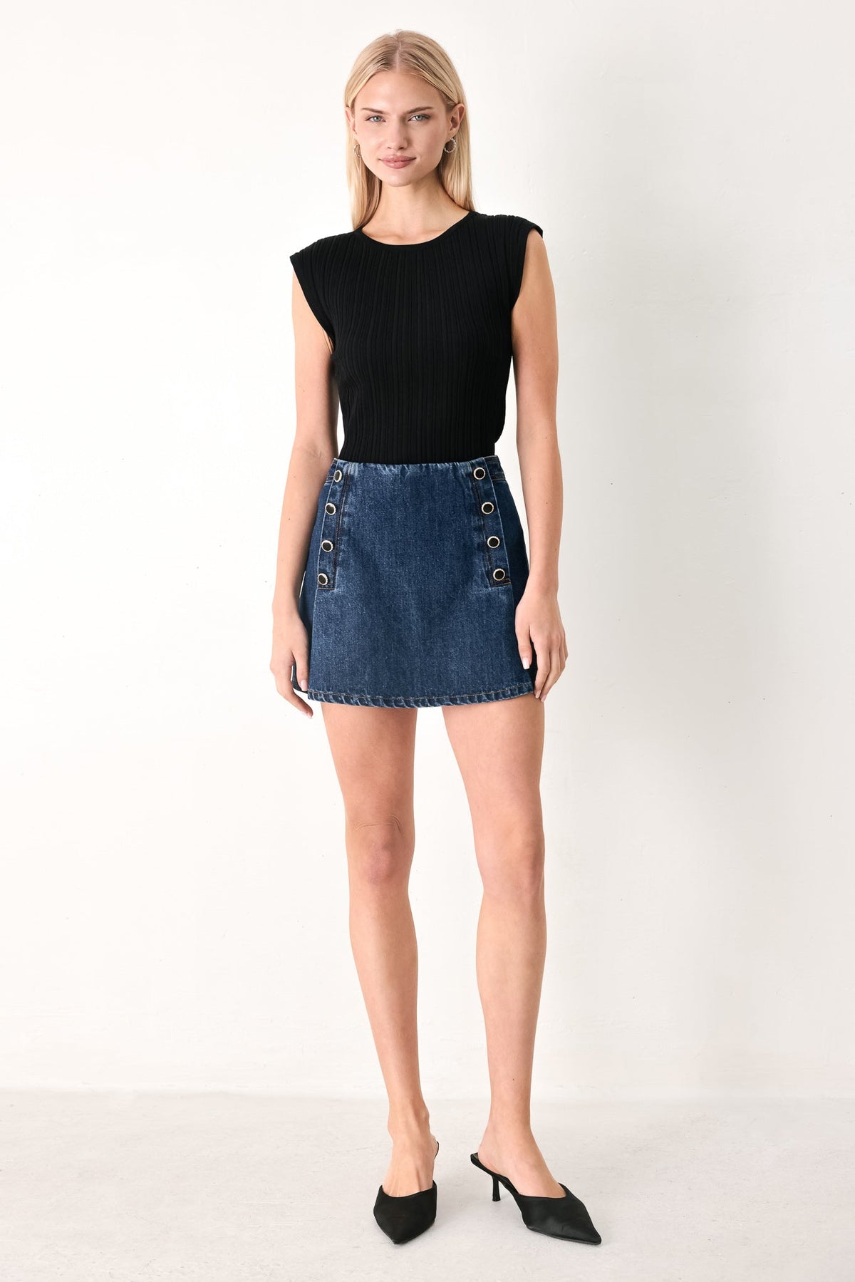 Woman wearing a black sleeveless top and denim skirt with button details on a white background