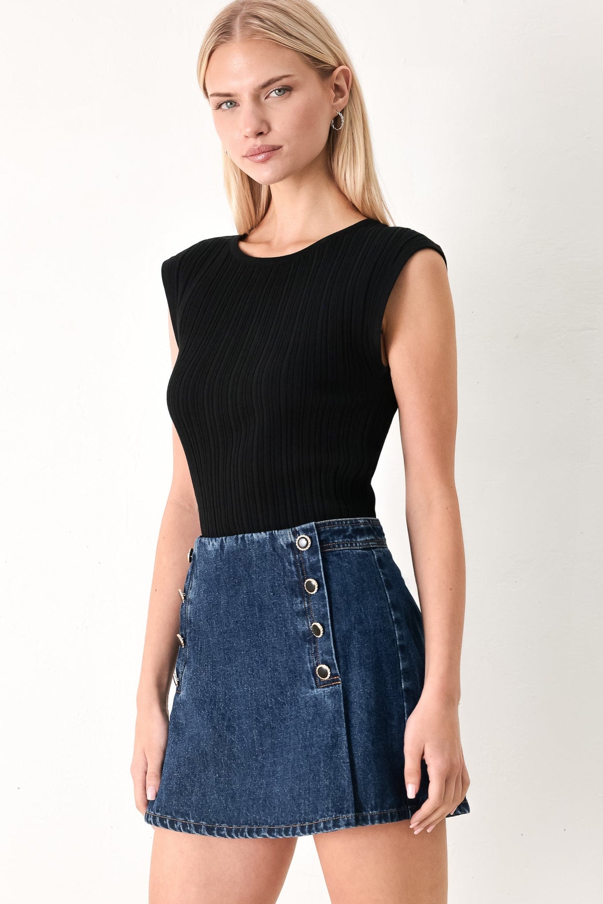 Woman wearing a black sleeveless top and blue denim skirt on a white background
