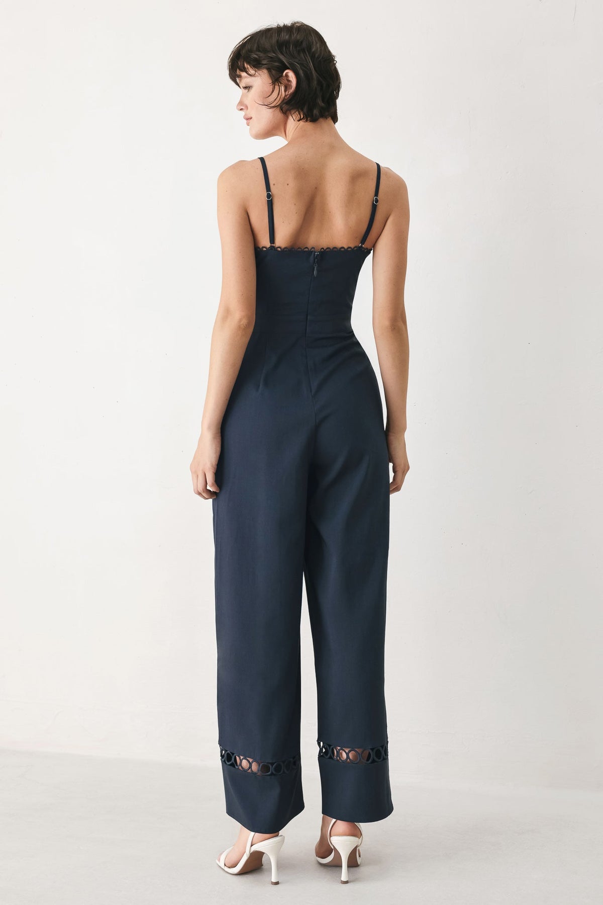 Woman wearing a navy blue jumpsuit with cut-out details on a white background