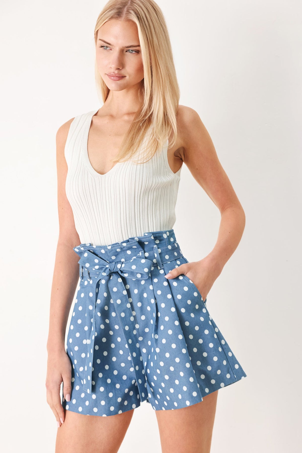 Woman wearing a white sleeveless top and blue polka dot shorts on a plain background