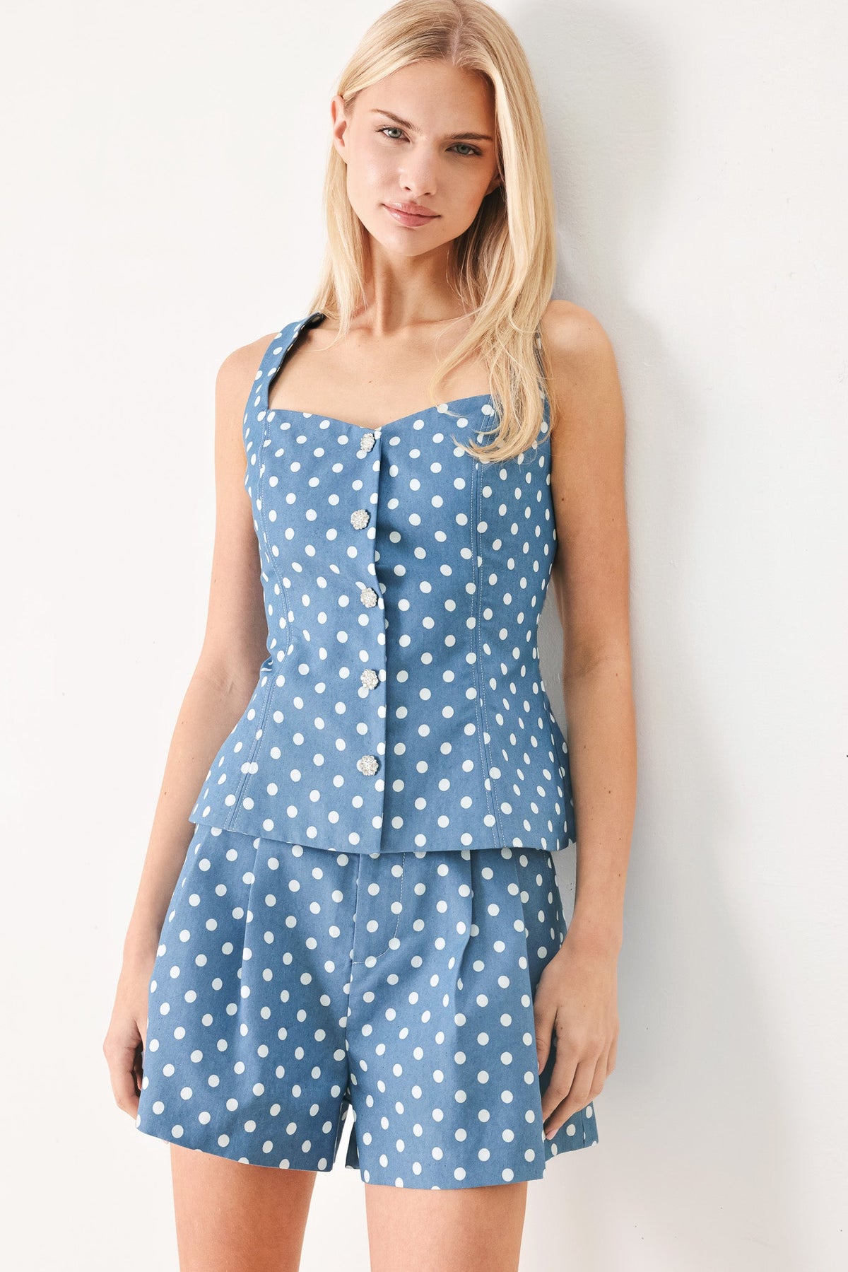 Woman wearing a blue polka dot top and shorts against a white background